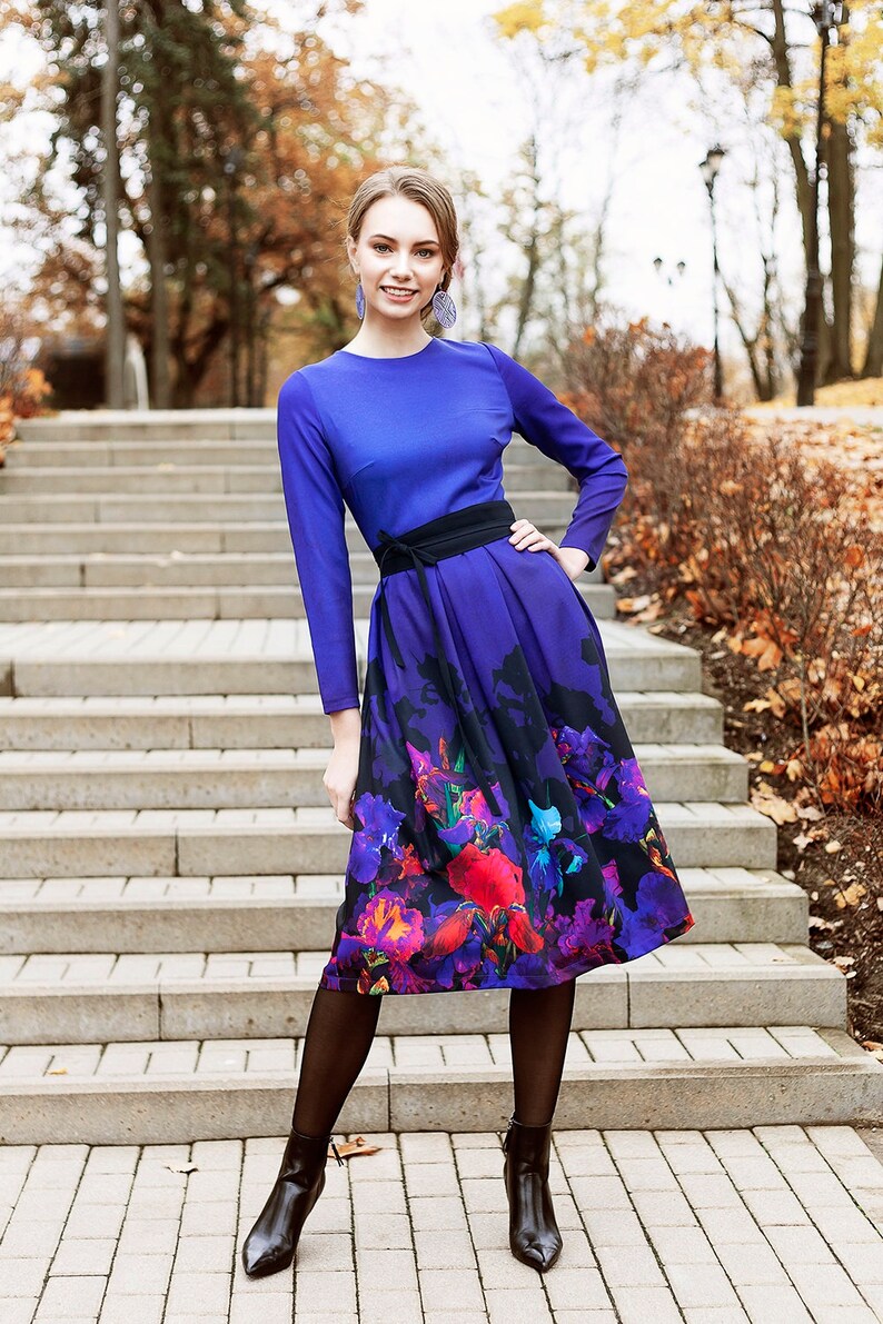 K&ouml;nnte beinhalten: Eine Frau in einem blauen Kleid mit einem Rock mit Blumenmuster und schwarzen Strumpfhosen. Sie steht auf einer Treppe vor einem Hintergrund aus Herbstlaub.
