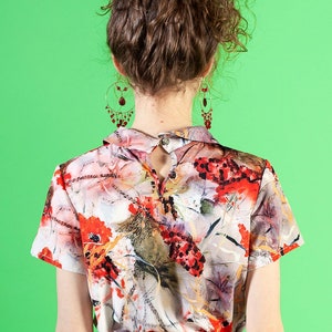 May include: A woman wearing a red skirt and a white blouse with a floral print. The blouse has a collar and short sleeves. The woman has curly brown hair and is wearing dangling earrings.