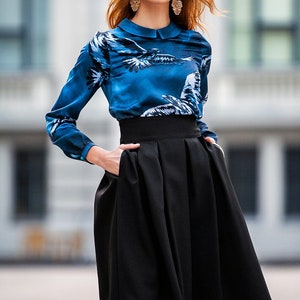 May include A woman wearing a blue and white patterned long-sleeved blouse with a black high-waisted skirt. She is wearing gold earrings.