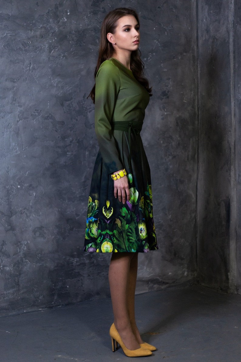 May include: A woman wearing a green dress with a floral print and yellow shoes. The dress has a fitted bodice and a full skirt.