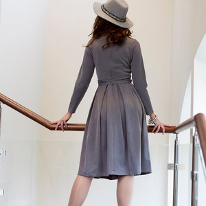 Puede incluir: Una mujer con un vestido gris, un sombrero gris y botas de tac&oacute;n gris. Est&aacute; de pie en una escalera con una barandilla de madera.
