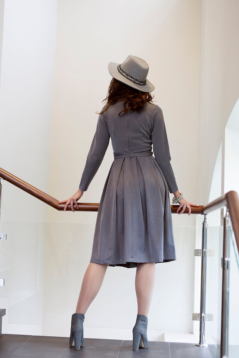 Puede incluir: Una mujer con un vestido gris, un sombrero gris y botas de tac&oacute;n gris. Est&aacute; de pie en una escalera con una barandilla de madera.