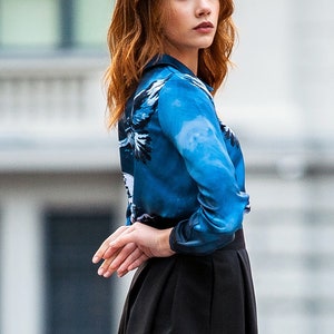 May include A woman wearing a blue and white patterned long-sleeve shirt with a black skirt.