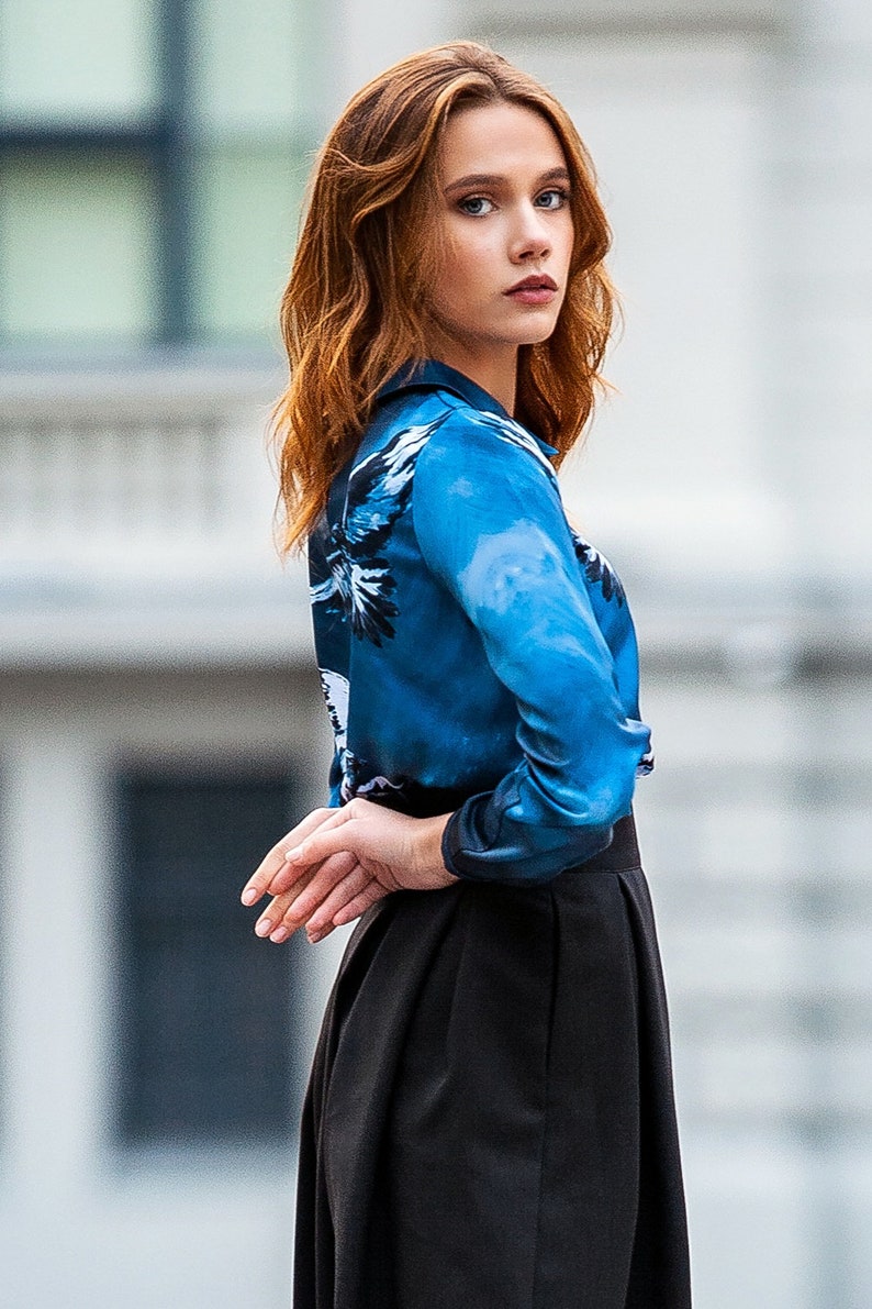 May include A woman wearing a blue and white patterned long-sleeve shirt with a black skirt.