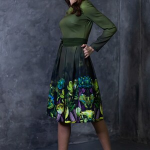 May include: A woman wearing a green dress with a floral print skirt and yellow heels. The dress has a green bodice and a dark green belt.