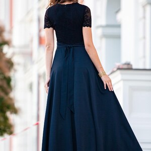 May include: A woman wearing a black lace top with a navy blue skirt. The skirt has a wide sash tied in a bow at the back.
