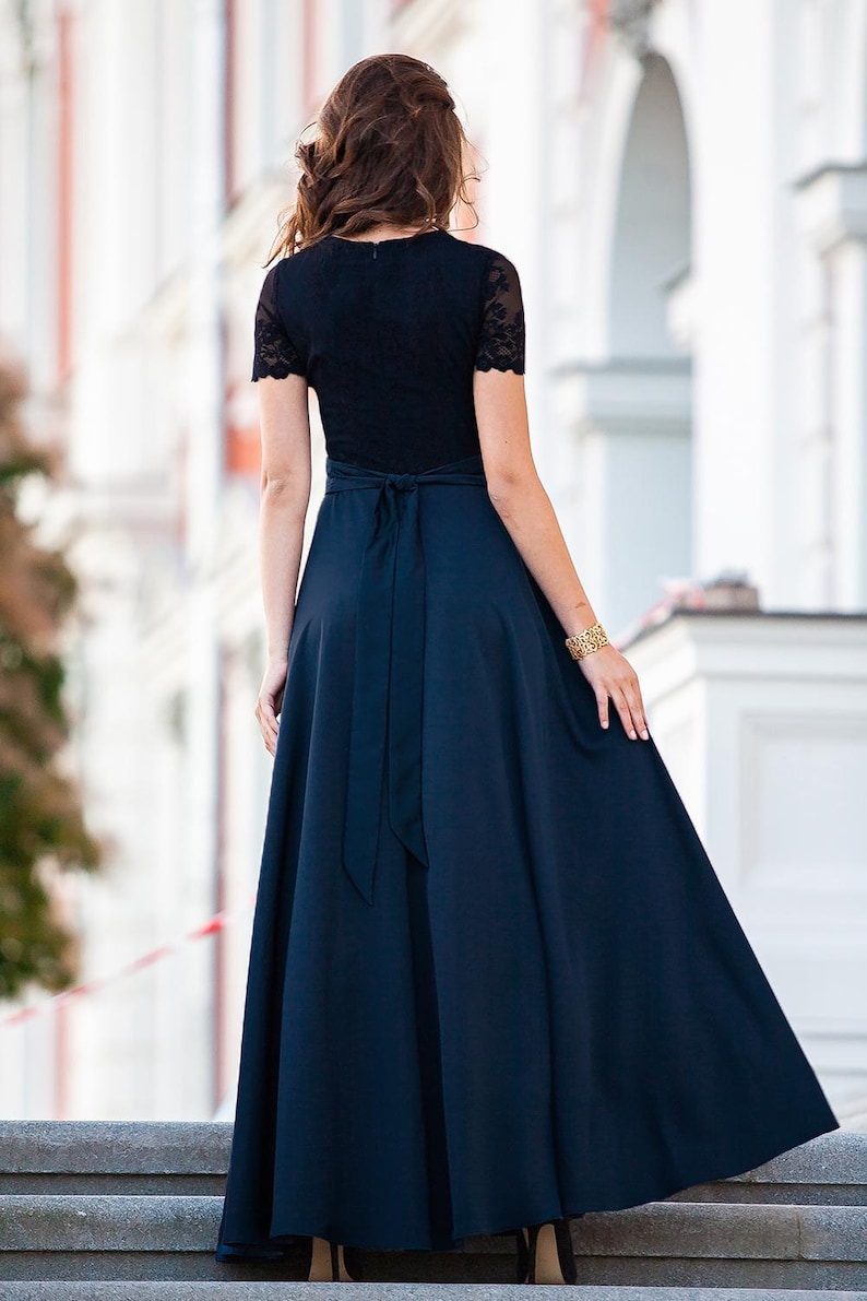 May include: A woman wearing a black lace top with a navy blue skirt. The skirt has a wide sash tied in a bow at the back.