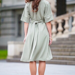 May include A sage green midi dress with a self-tie belt and short sleeves. The dress is fitted at the waist and flows out to a slightly flared skirt.