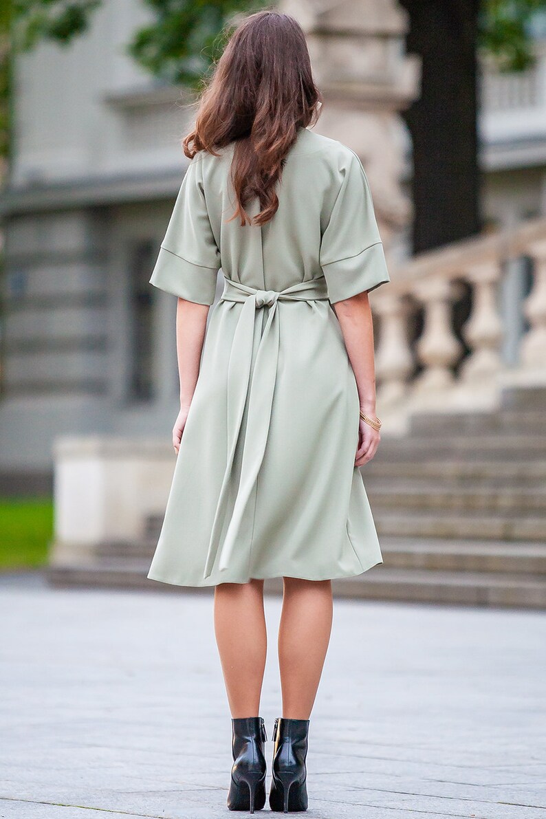 May include A sage green midi dress with a self-tie belt and short sleeves. The dress is fitted at the waist and flows out to a slightly flared skirt.