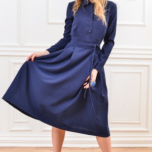 Pu&ograve; includere: Un abito midi blu navy con colletto, maniche lunghe e cintura annodata in vita.