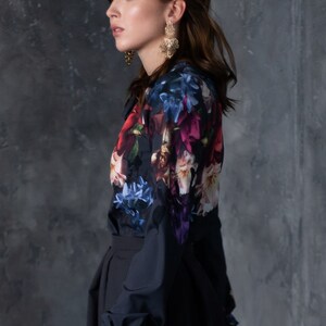 May include: A woman wearing a black long-sleeved blouse with a floral print and a black skirt. She is wearing gold earrings.