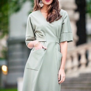 May include A sage green midi dress with a v-neckline, short sleeves, and two large pockets. The dress has a fitted waist and a flowy skirt.