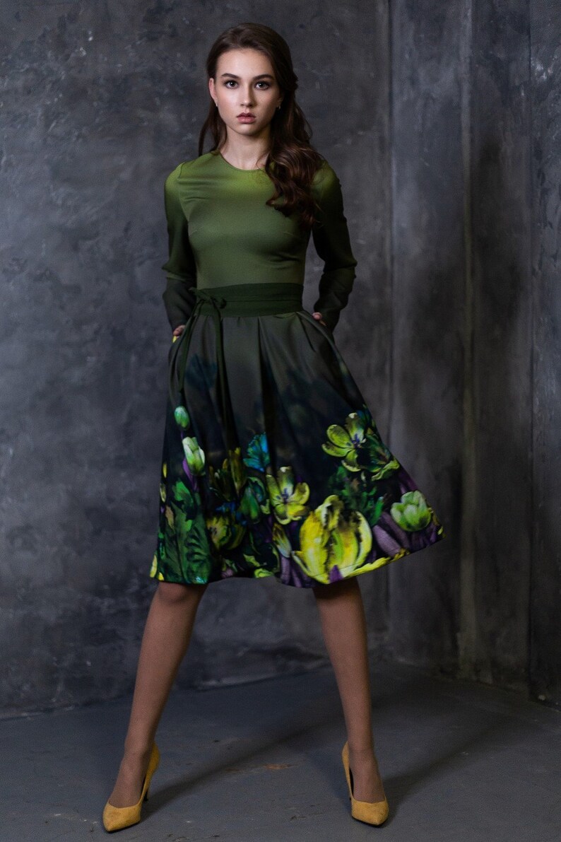 May include: A woman wearing a green dress with a floral print skirt. The dress has a fitted bodice and a full skirt. She is wearing yellow heels.