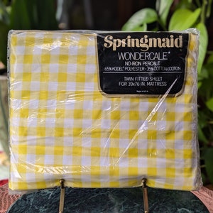 May include: A yellow and white checkered twin fitted sheet in a plastic package. The package has a label that reads "Springmaid Wondercale No-Iron Percale 65% Kodel Polyester - 35% Cotton/Coton Twin Fitted Sheet for 39x76 in. Mattress."
