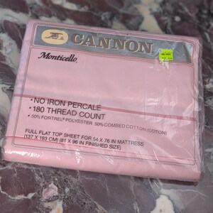 May include: A pink Cannon Monticello full flat top sheet in original plastic packaging. The label specifies 180 thread count, no iron percale, and a blend of 50% Fortrel polyester and 50% combed cotton for a 54 x 76 inch mattress.