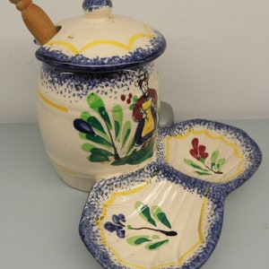 May include: A ceramic condiment set featuring a lidded jar with a wooden spoon and a two-section serving dish. The set is painted with blue, yellow, green, and red floral and figurative designs. The jar is approximately 6 inches tall.