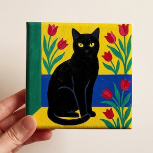 May include: A square painting featuring a black cat with yellow eyes, sitting in front of a yellow background with red tulips and green stems. A blue stripe is behind the cat. The painting has a green border.