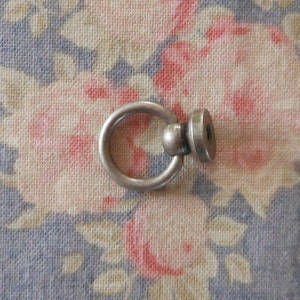 Può includere: Anello in metallo argentato con una sfera rotonda e un disco piatto attaccati. L'anello ha un diametro di circa 2,5 cm.