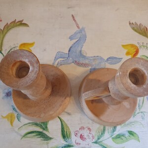 May include: Two wooden candle holders with a simple design. The holders are made of light brown wood and have a round base. The holders are perfect for adding a touch of rustic charm to any home.