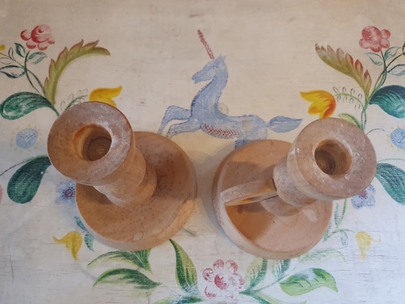 May include: Two wooden candle holders with a simple design. The holders are made of light brown wood and have a round base. The holders are perfect for adding a touch of rustic charm to any home.