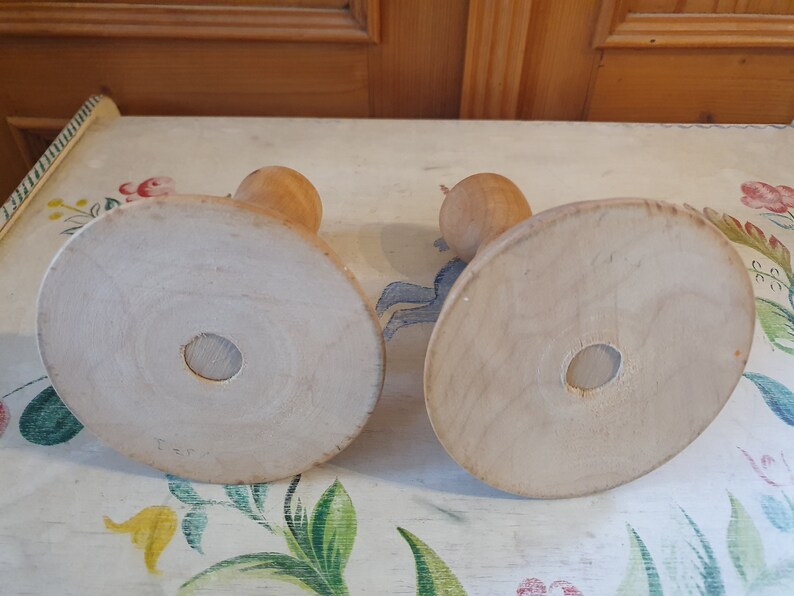 May include: Two wooden candle holders with round bases. The bases are plain and light brown. The candle holders are made of wood and have a simple design.