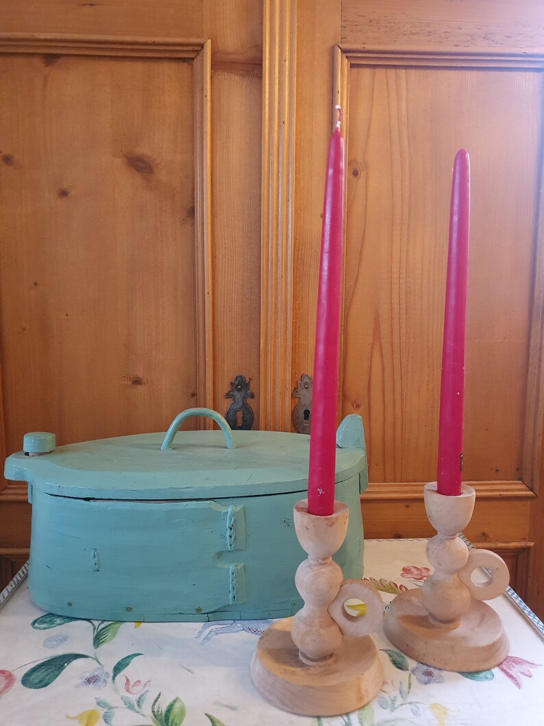 May include: Two wooden candle holders with red candles, and a teal painted wooden box with a lid on a floral tablecloth.