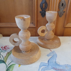May include: Two wooden candle holders with a ring handle. The candle holders are made of light brown wood and have a simple design.