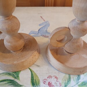 May include: Two wooden candle holders with a unique design. The holders are made of light brown wood and have a simple, elegant design.
