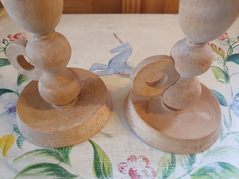May include: Two wooden candle holders with a unique design. The holders are made of light brown wood and have a simple, elegant design.