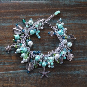 May include: A silver charm bracelet with a variety of blue and green beads, charms, and a starfish pendant.