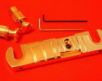 Puede incluir: Un puente de guitarra de color dorado con dos clavijas de afinación doradas y dos llaves Allen. El puente tiene un diseño en forma de U con una serie de ranuras.