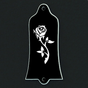 Puede incluir: Placa negra para la pala de la guitarra con un dise&ntilde;o de rosa blanca. La rosa est&aacute; detallada con p&eacute;talos y hojas. La placa tiene dos agujeros de montaje y bordes lisos. El fondo es negro.