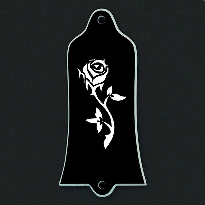 Puede incluir: Placa negra para la pala de la guitarra con un dise&ntilde;o de rosa blanca. La rosa est&aacute; detallada con p&eacute;talos y hojas. La placa tiene dos agujeros de montaje y bordes lisos. El fondo es negro.