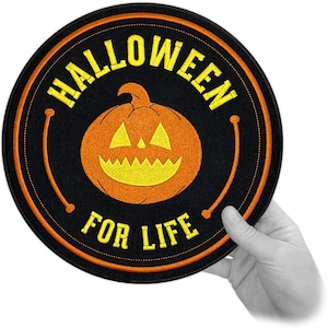 Op de afbeelding: Een ronde zwarte patch met de woorden "HALLOWEEN FOR LIFE" in het geel. De patch heeft een oranje pompoen in het midden. De patch wordt door een hand vastgehouden.