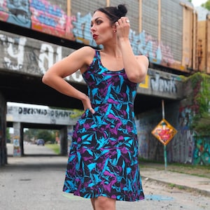 Puede incluir: Un vestido sin mangas con fondo negro y un patrón de murciélagos azules y morados. El vestido tiene un escote redondo y una falda acampanada.