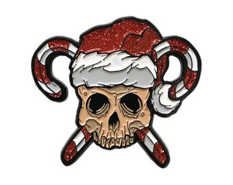 May include: A red and white enamel pin featuring a skull wearing a red glitter Santa hat and holding two candy canes crossed in front of it.