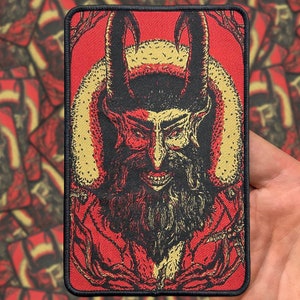 May include: A red and black embroidered patch featuring a horned, bearded figure with a sinister grin. The figure is wearing a fur-trimmed hat and is surrounded by a red and gold background.