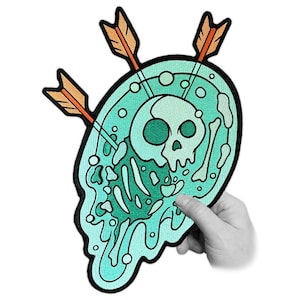 May include: Embroidered patch with a teal skull design, bones, and arrows. The patch has a black border and is held by a hand. The arrows have orange fletching. The skull is in the center of a teal blob.