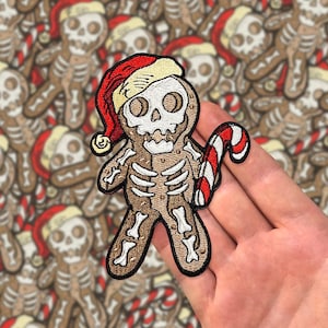 May include: A gingerbread man with a skull face and a candy cane in its hand. The gingerbread man is wearing a red and white Santa hat.