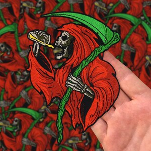 Può includere: Una toppa ricamata che rappresenta la Morte, vestita di rosso, che tiene una falce verde e beve da una lattina gialla.