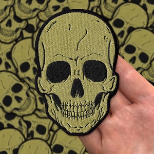 Puede incluir: Un parche de calavera bordado de color verde con ojos negros y una sonrisa de dientes.