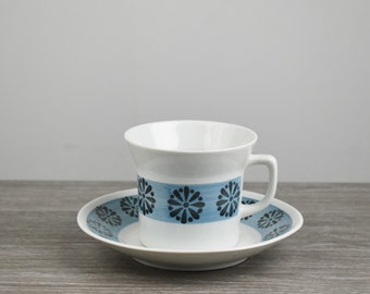 Puede incluir: Una taza de té y un platillo blancos con un patrón floral azul y negro. La taza tiene un borde acampanado y un asa. El platillo tiene un patrón a juego.