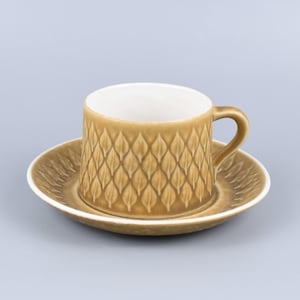 Könnte beinhalten: Eine braune Kaffeetasse und Untertasse aus Keramik mit einem Blattmotiv. Die Tasse hat ein weißes Innenleben und einen Henkel.