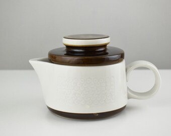 May include: White ceramic teapot with a brown lid and a white floral pattern. The teapot has a brown band around the bottom and a brown handle.