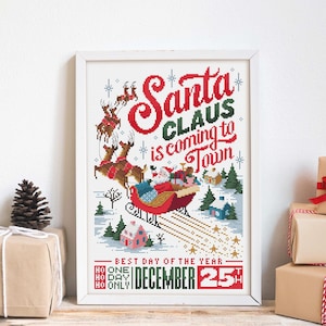 May include: A framed cross-stitch design with the text "Santa Claus is coming to Town." The image depicts Santa in a sleigh pulled by reindeer, with a snowy landscape and the date "December 25th."
