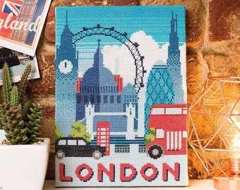 May include: A cross-stitch artwork depicting a London skyline with iconic landmarks like the London Eye, Big Ben, and a red double-decker bus. The artwork is framed and has the word "LONDON" written in red and white letters at the bottom.