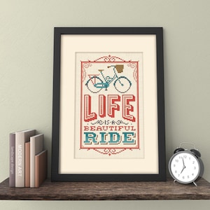May include: A framed print featuring a vintage-style illustration of a bicycle and the text "Life is a beautiful ride". The print has a white background with a red, blue, and green colour scheme.