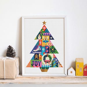 May include: A framed Christmas tree picture with a white frame. The tree is made up of colourful geometric shapes and festive icons, such as a snowman, angel, and ice skate. The word "JOY" is at the base, and a gold star sits at the top.