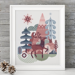 Op de afbeelding: Een kruissteekpatroon met een gestileerde hert in een winters boslandschap. Het hert is bruin met een witte kraag en gewei. Het bos bestaat uit blauwe en groene bomen, een roze berg en een blauwe lucht met een witte zon.