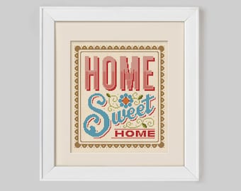 May include: A white framed cross-stitch with a brown background and a colorful design that says "Home Sweet Home" with a flower in the middle.